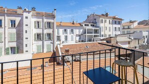 Une terrasse sur le toit, avec une table et des chaises, entourée d’immeubles aux façades blanches et aux toits recouverts de tuiles rouges.