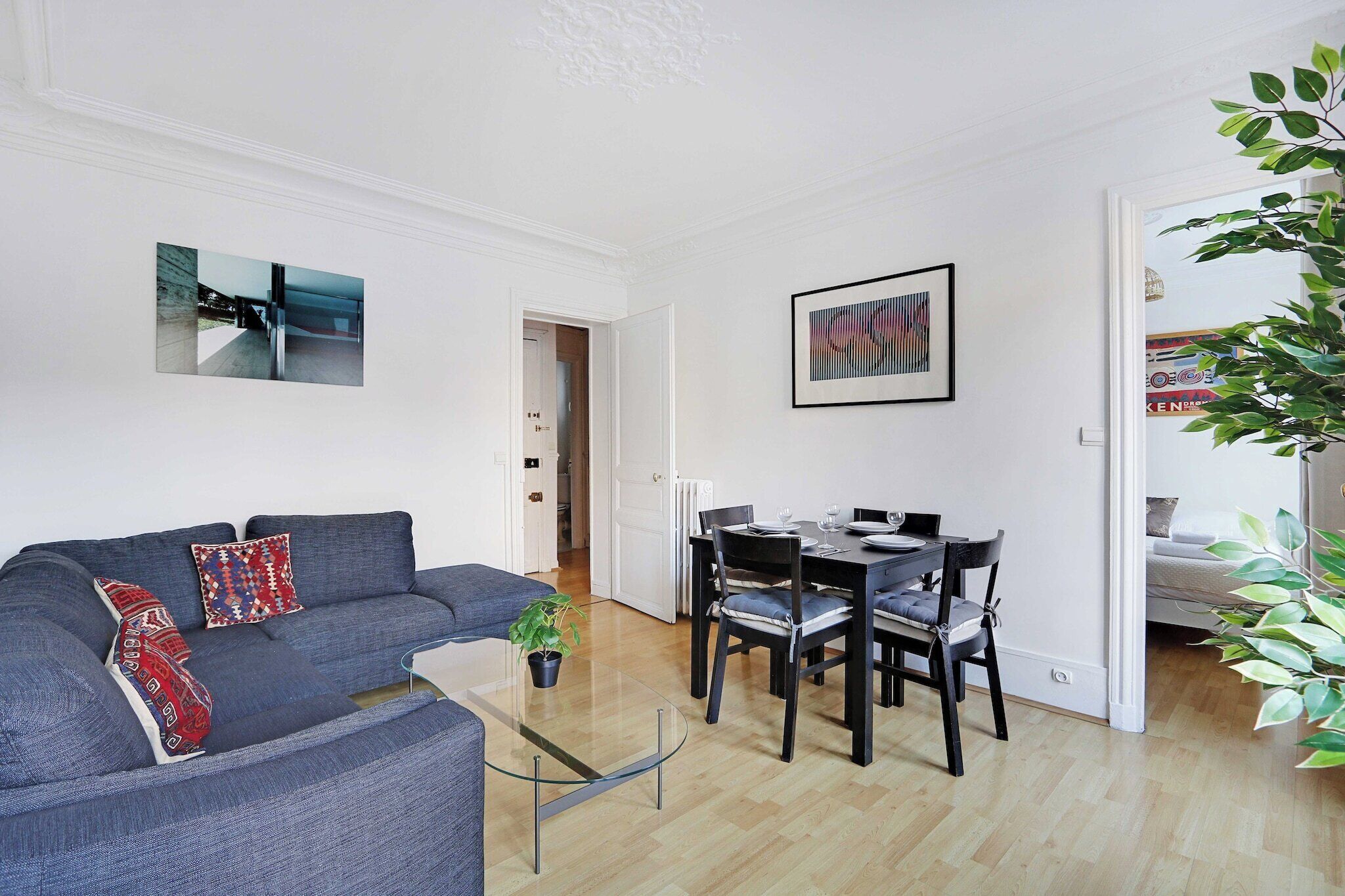 Ein modernes Wohnzimmer mit einem grauen Sofa, einem Glastisch und einem Essbereich mit einem schwarzen Tisch und Stühlen.