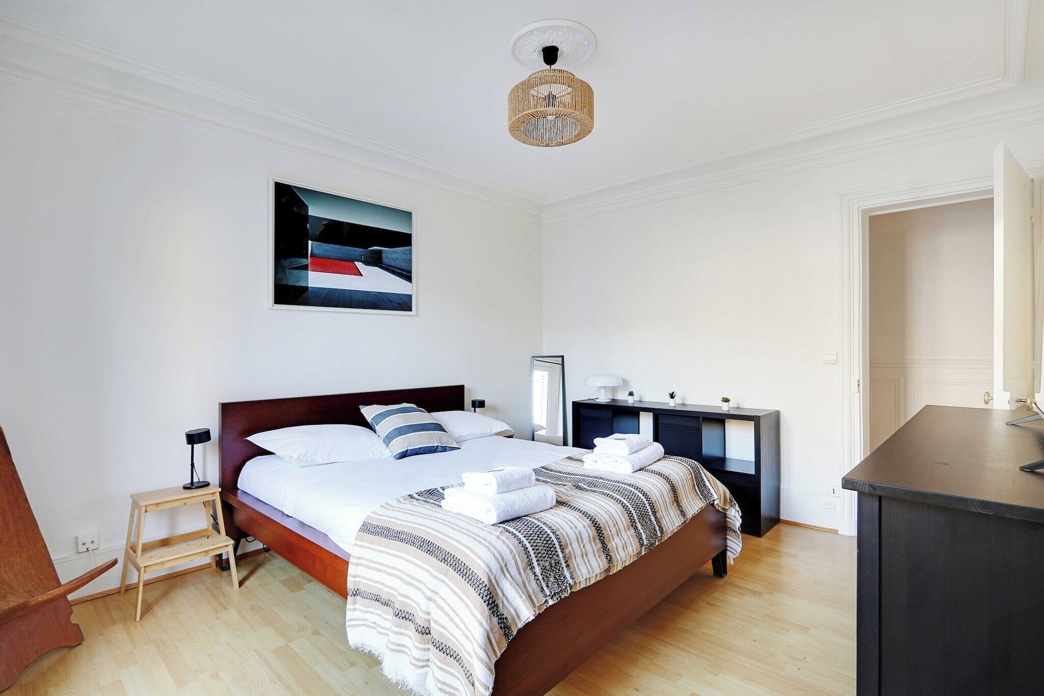 Ein ordentlich eingerichtetes Schlafzimmer mit einem Bett, Nachttischen, einem kleinen Holzschemel und einer Pendelleuchte.