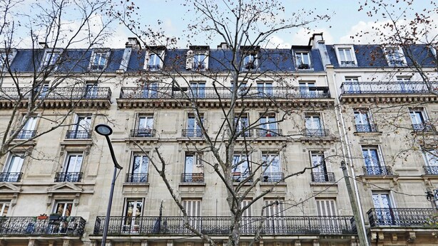 A multi-story building with balconies, a street lamp, and a tree in front.