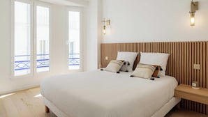 Un dormitorio con una cama grande, cabecera de madera, dos mesitas de noche y vistas a un balcón a través de las ventanas.