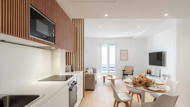 Una cocina moderna con microondas integrado, un comedor con mesa preparada para dos personas y un televisor montado en la pared.