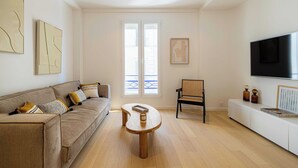 Una sala de estar moderna con un sofá, una mesa de centro de madera, una silla, un televisor y un balcón con vistas.