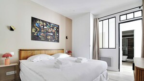A hotel room with a large bed, a painting on the wall, and a view of the bathroom through an open door. - Charming aptt with patio - 2BD/4P - Monceau Park (Paris)