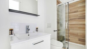 A modern bathroom with a white vanity, a glass shower enclosure, and a wooden floor. - Charming aptt with patio - 2BD/4P - Monceau Park (Paris)
