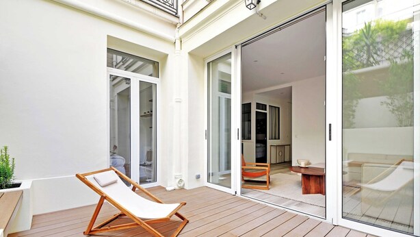 A wooden deck with a lounge chair and a small table, a sliding glass door leading to an interior space with a sofa and a coffee table. - Charming aptt with patio - 2BD/4P - Monceau Park (Paris)