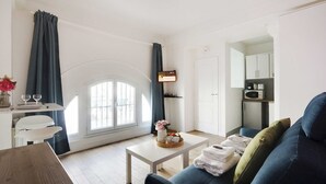A modern living room with a sofa, a coffee table, and a dining area with a table set for two. - Atypical Bright Studio - 2P - Gare du Nord (Paris)
