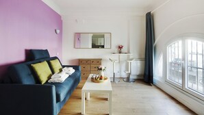 A modern living room with a blue sofa, a white coffee table, and a pink accent wall. - Atypical Bright Studio - 2P - Gare du Nord (Paris)