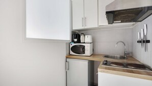 A compact kitchen with white cabinets, a microwave, a coffee maker, and a sink. - Atypical Bright Studio - 2P - Gare du Nord (Paris)