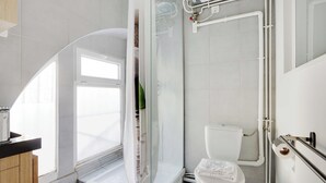 A modern bathroom with a glass shower enclosure, a toilet, and a sink with a wooden cabinet. - Atypical Bright Studio - 2P - Gare du Nord (Paris)