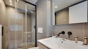 Ein modernes Badezimmer mit einer Duschkabine aus Glas, einem weißen Waschbecken und einem Spiegel darüber.