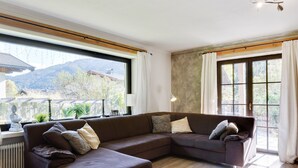 A modern living room with a sectional sofa, large windows, and a view of a mountainous landscape. - Chalet Leogang near Skilift & Bikepark (Leogang)