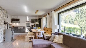 A modern kitchen with a dining area, a sofa, and a large window with a view of trees. - Chalet Leogang near Skilift & Bikepark (Leogang)
