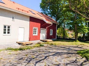 Een gebouw met twee verdiepingen, een rode gevel en witte details, een voortuin en een geplaveid oprit.