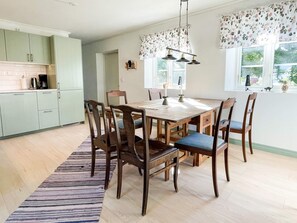 Een eetgedeelte met een houten tafel en stoelen, een gestreept vloerkleed, en een keuken op de achtergrond.