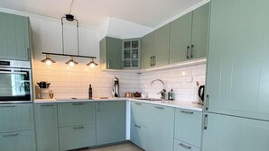 Una cocina moderna con gabinetes verde claro, azulejos tipo metro blancos y una campana extractora de acero inoxidable.