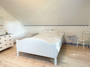 Een slaapkamer met een enkel bed, een dressoir, een stoel en een klein tafeltje.