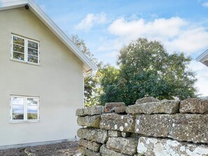 Een gebouw met twee verdiepingen, een stenen muur en een boom op de achtergrond.