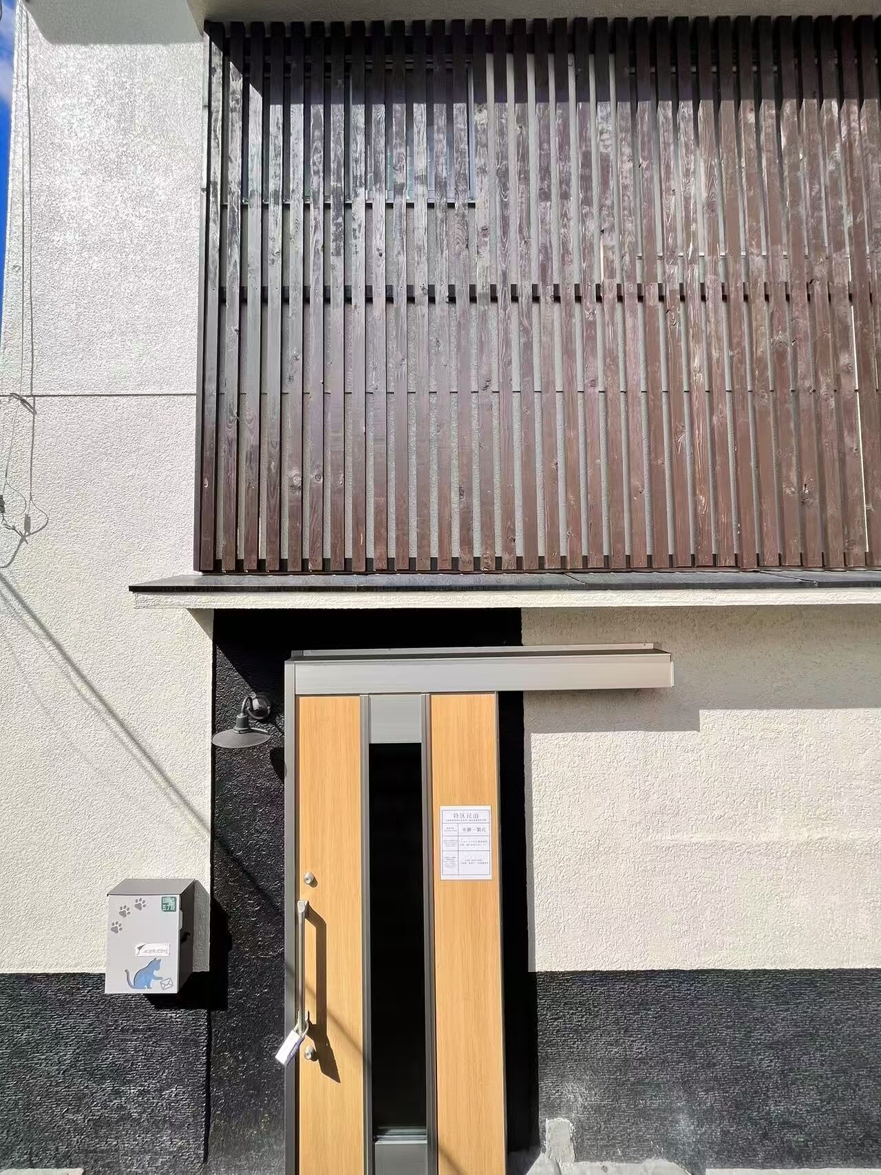 A building with a wooden slatted roof, a door with a handle, and a small sign on the wall.