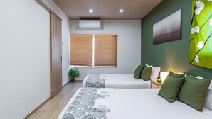 Une chambre d’hôtel avec deux lits, un plafond en bois, un appareil de climatisation, une fenêtre avec des stores, un mur vert et un tableau.