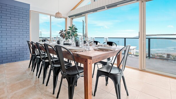 A dining area with a wooden table set for six, black chairs, and a view of the sea through large windows. - Retreat by the Sea – Coastal Escape with Cozy Spa & Panoramic Ocean Sunset Views (Gerroa)