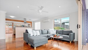 A modern living room with a grey sectional sofa, a round coffee table, and a ceiling fan. - Retreat by the Sea – Coastal Escape with Cozy Spa & Panoramic Ocean Sunset Views (Gerroa)