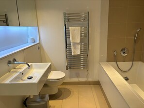 Moderni kylpyhuone, jossa on pesuallas, wc ja kylpyamme.