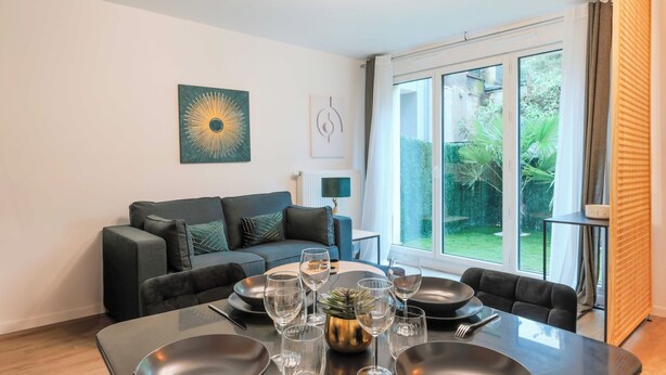 Una sala moderna con una mesa de comedor preparada para seis comensales, un sofá y un ventanal con vistas a la vegetación.