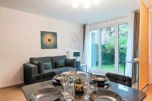 Een moderne woonkamer met een eettafel voor zes personen, een bank en een groot raam met uitzicht op groen.