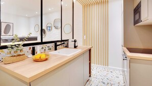 A modern bathroom with a large mirror, a sink, and a countertop with decorative items. - Magnificent Apartment 1BR/4P - Arc de Triomphe (Neuilly-sur-Seine)