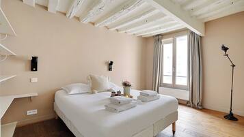 Une chambre à coucher avec un lit, des tables de chevet, une commode, une lampe et une fenêtre avec des rideaux.