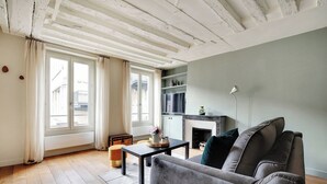A living room with a grey sofa, a small table with a vase, and a fireplace. - Chic apartment -1BR/4P- Haut Marais / République (Paris)