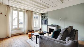 Un salon avec un canapé gris, une petite table sur laquelle est posé un vase, et une cheminée.