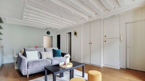 A modern living room with a grey sofa, a black coffee table, and two yellow ottomans. - Chic apartment -1BR/4P- Haut Marais / République (Paris)
