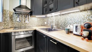 A modern kitchen with black cabinets, a tiled backsplash, a stainless steel oven, a sink, and a coffee maker. - Chic apartment -1BR/4P- Haut Marais / République (Paris)