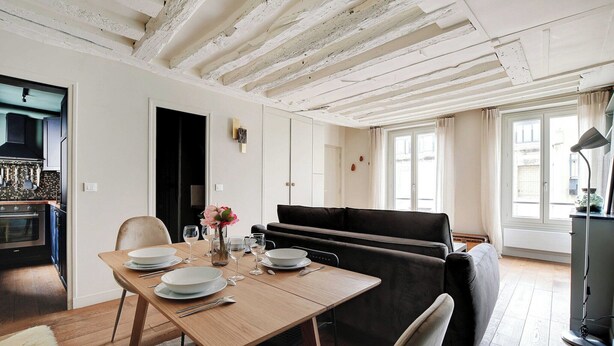 A dining area with a wooden table set for four, a black sofa, and a kitchen visible in the background. - Chic apartment -1BR/4P- Haut Marais / République (Paris)