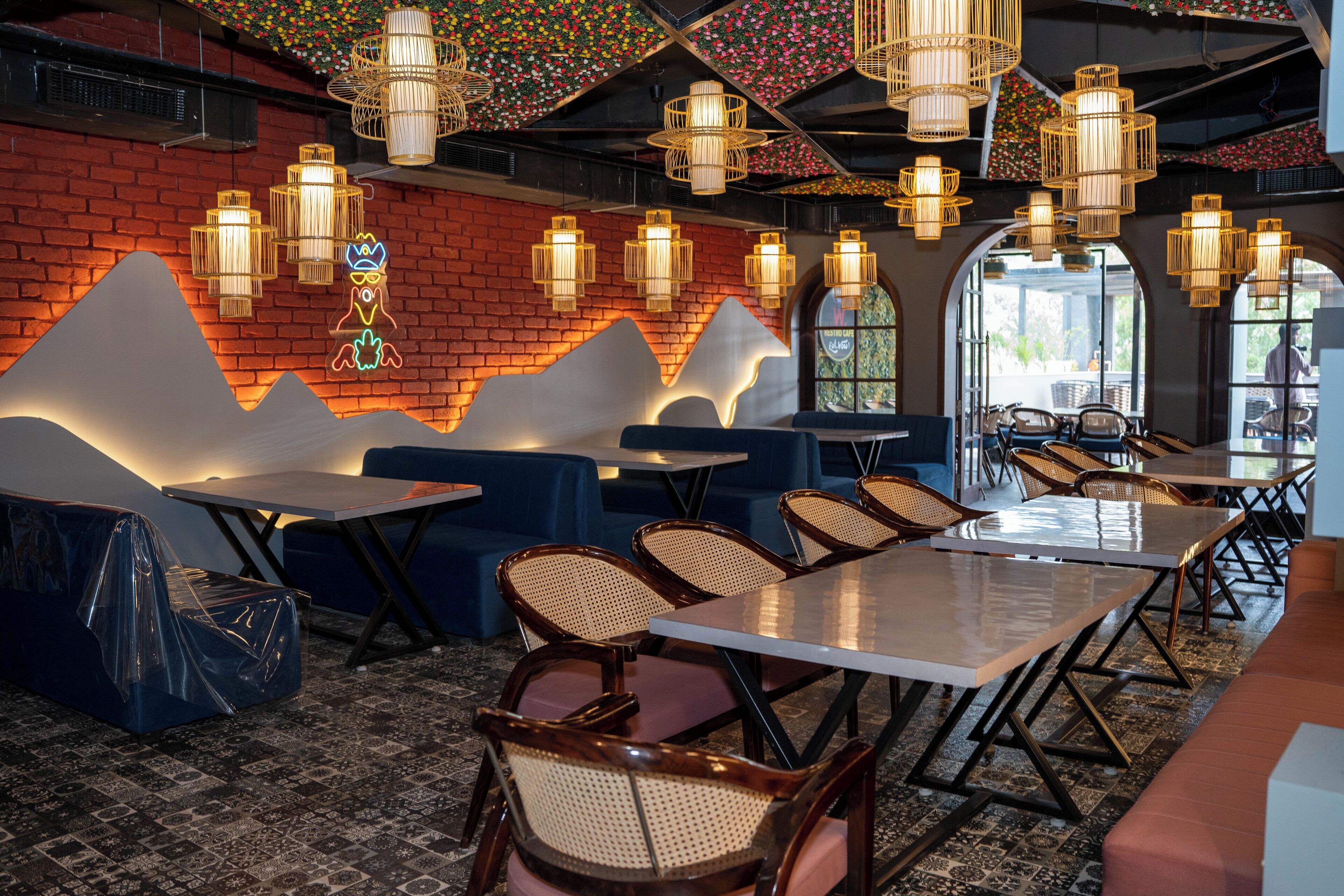 Interior de restaurante con pared de ladrillo, mesas de madera, asientos acolchados y lámparas colgantes.