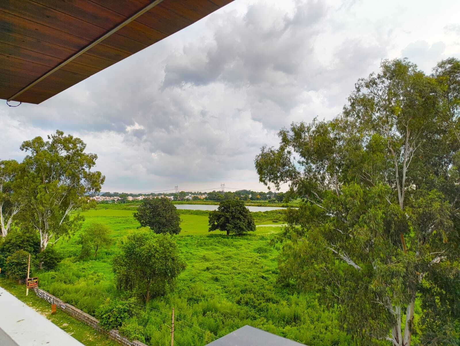A view from a covered balcony overlooking a lush green landscape with trees and a distant body of water.