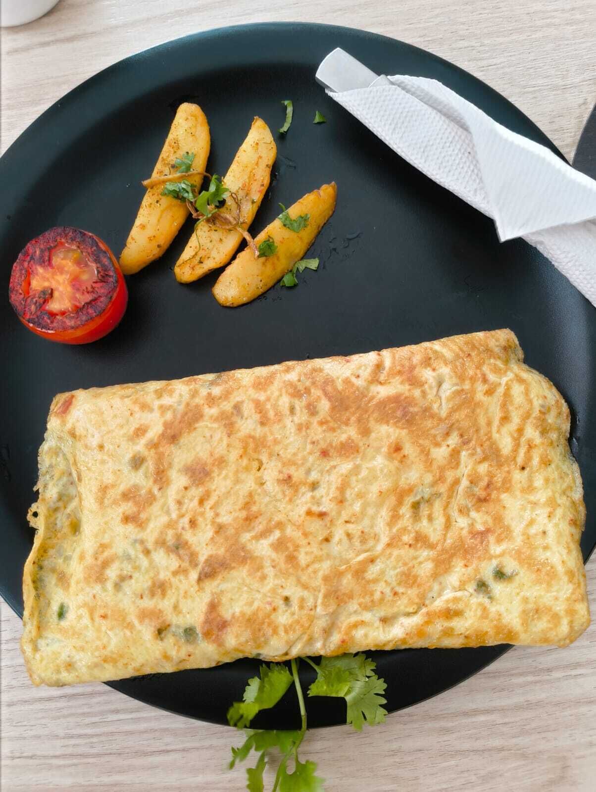 Une assiette contenant une omelette repliée, des pommes de terre rôties et une tomate grillée.