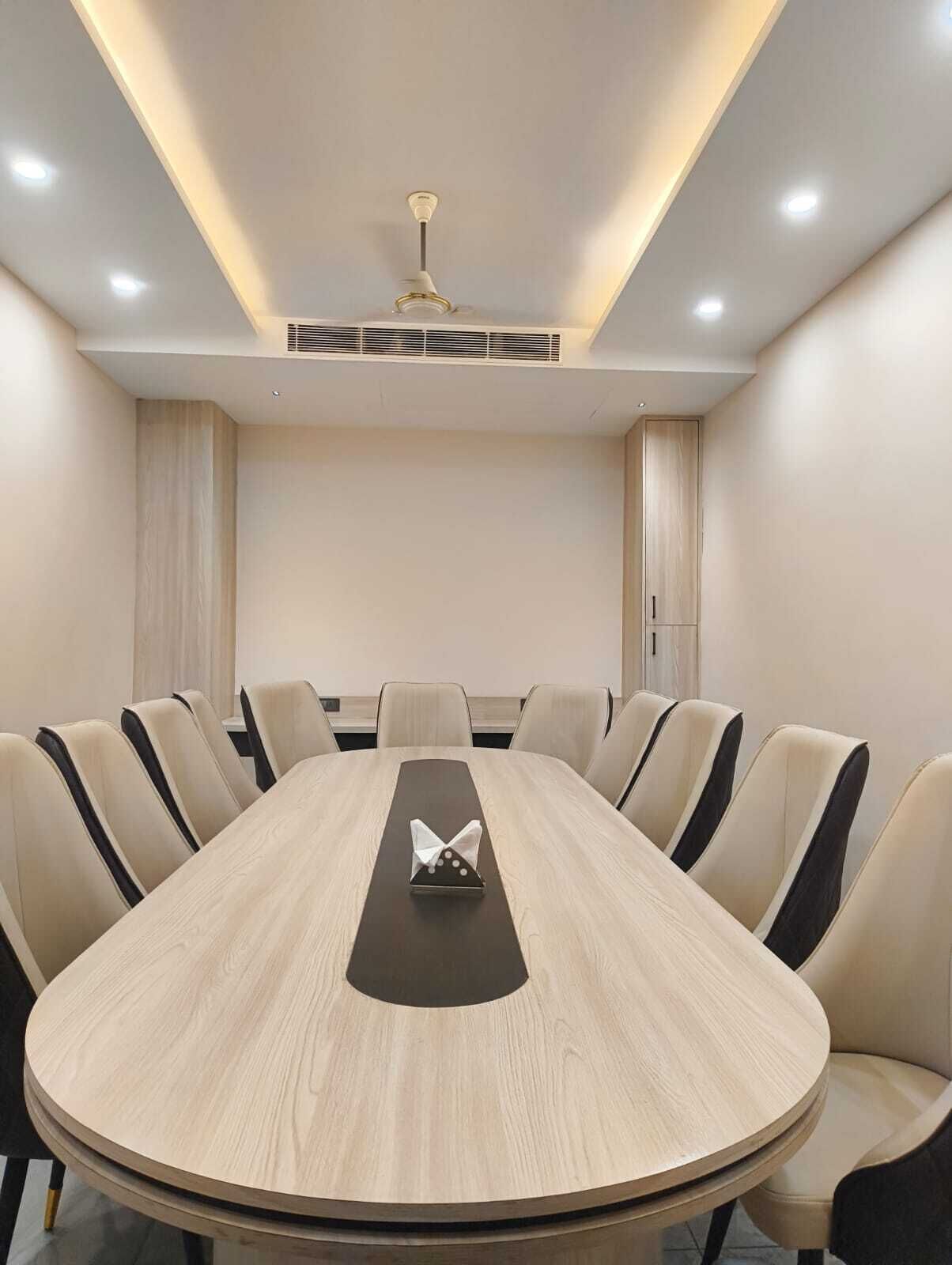 Une salle de conférence avec une table ronde, des chaises de couleur beige et un ventilateur de plafond.