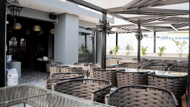 A rooftop restaurant with wicker chairs and tables, outdoor lighting, and a view of the cityscape. - Hotel W Grand - A Boutique Hotel (Haridwar)