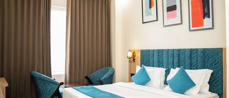 A hotel room with a large bed, two chairs, a wooden nightstand, and a wall-mounted lamp.
