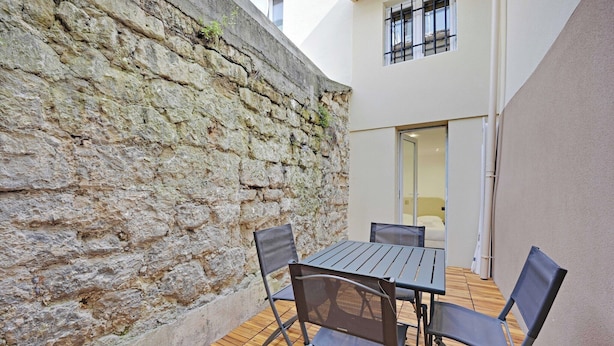 A patio with a stone wall, a table, and four chairs. - Modern apartment with terrace (Aubervilliers)