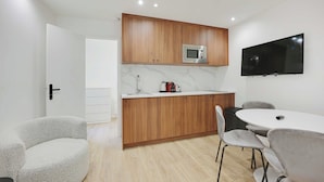 A modern kitchen with wooden cabinets, a built-in microwave, and a flat-screen TV. There is a dining area with a round table and grey chairs. - Modern apartment with terrace (Aubervilliers)