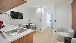 A modern kitchen with a built-in sink, a dining area with a round table and chairs, and a TV mounted on the wall. - Modern apartment with terrace (Aubervilliers)
