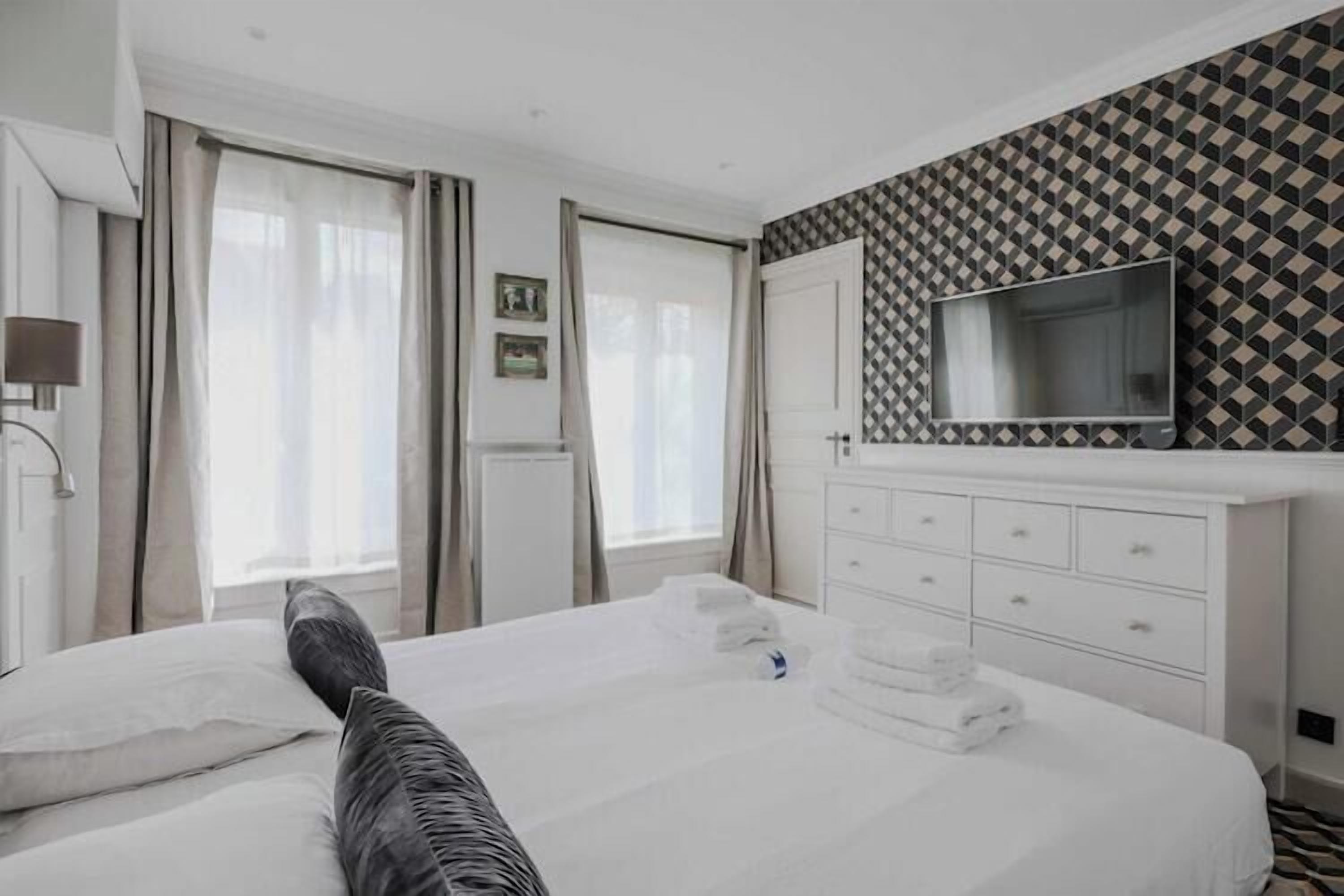 A hotel room with a bed, a TV mounted on the wall, and a window with curtains.