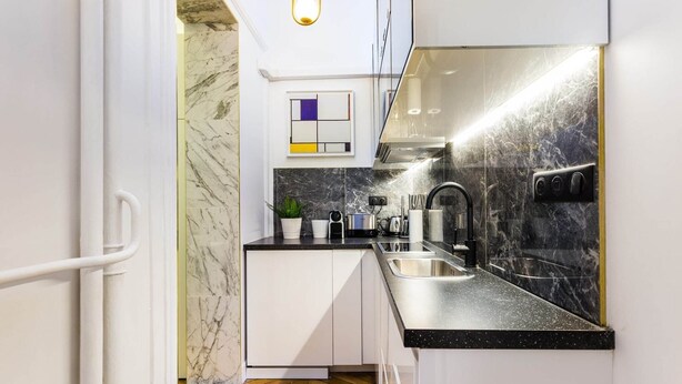 A compact kitchen with white cabinets, a black countertop, and a marble backsplash. - Moderne apartment - 1BR/4P - AC - Champs-Élysées (Paris)