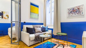 A modern living room with a white sofa, a glass partition, a small round table, and a colorful rug. - Moderne apartment - 1BR/4P - AC - Champs-Élysées (Paris)