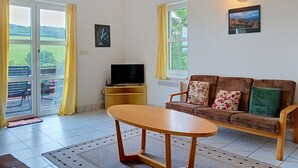 A living room with a sofa, a table, a TV, and a window with curtains. - Green Valley Park Stárkov 13 by Interhome (Stárkov)