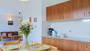 A dining area with a wooden table set for four, a vase with flowers, and a kitchen with wooden cabinets and a coffee maker. - Green Valley Park Stárkov 13 by Interhome (Stárkov)